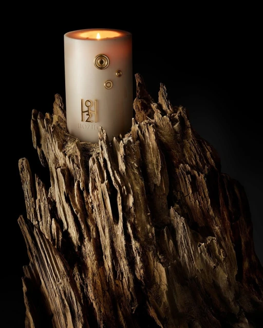 Lit candle on a textured, gold-colored wooden pedestal against a dark background creates a warm and inviting ambience.