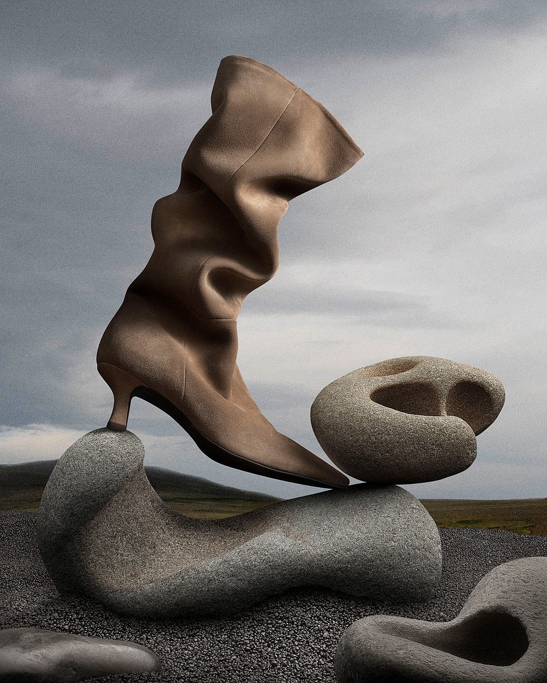 A beige suede slouch boot is balanced on natural, carved-out rocks against a cloudy sky backdrop in a fashion-forward still life image.