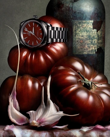 Still life photography by Peter Lippmann featuring a luxury wristwatch resting on dark red tomatoes beside weathered metal bottle