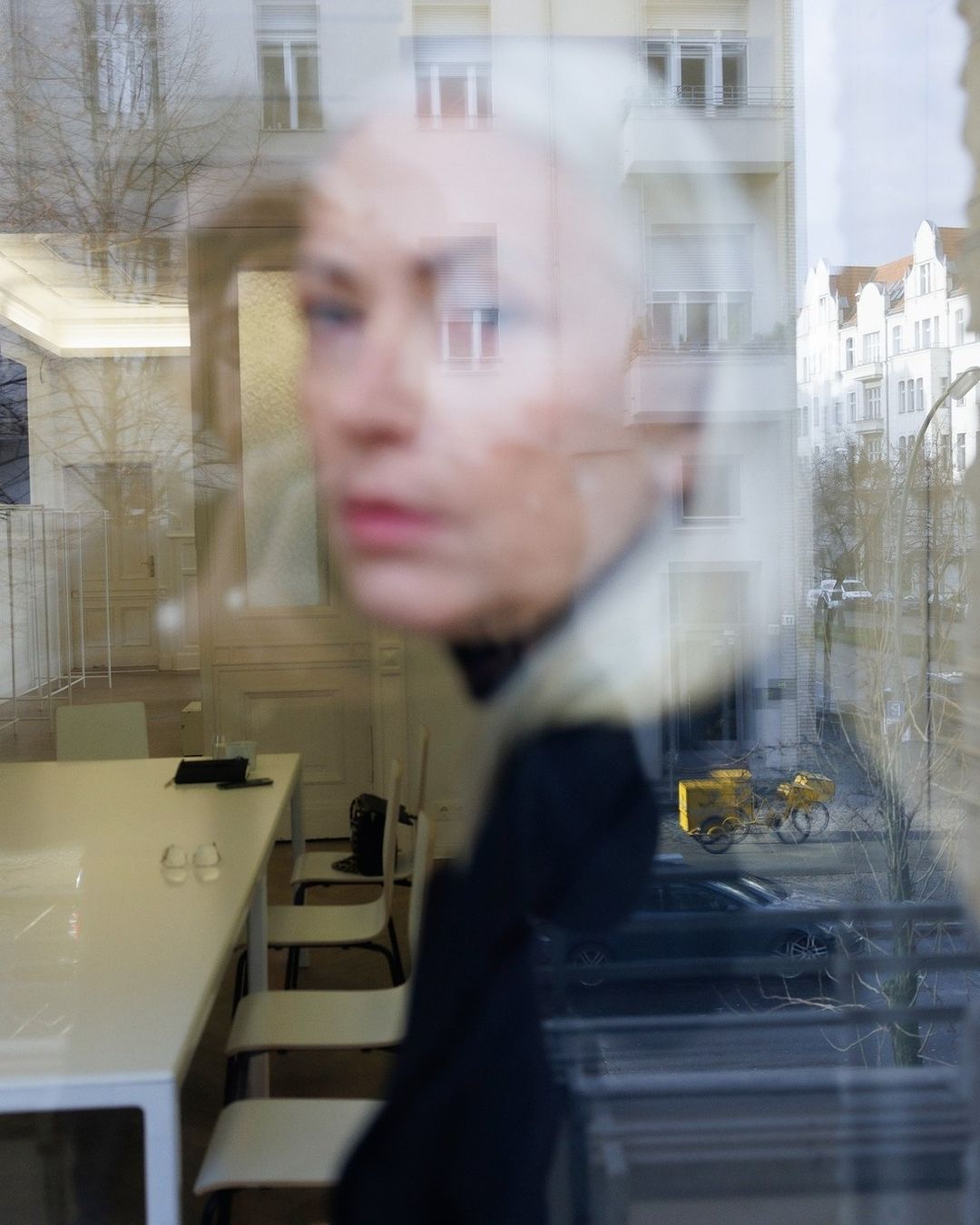 Abstract view through a window with a woman's face reflecting, office space, street, and building blending together in a unique composition.