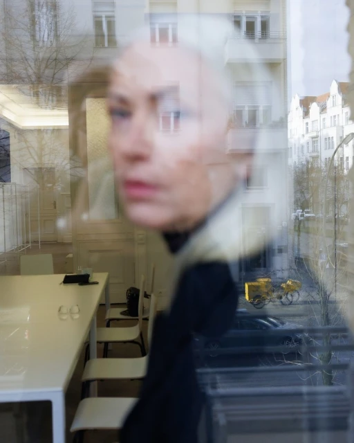 Abstract view through a window with a woman's face reflecting, office space, street, and building blending together in a unique composition.