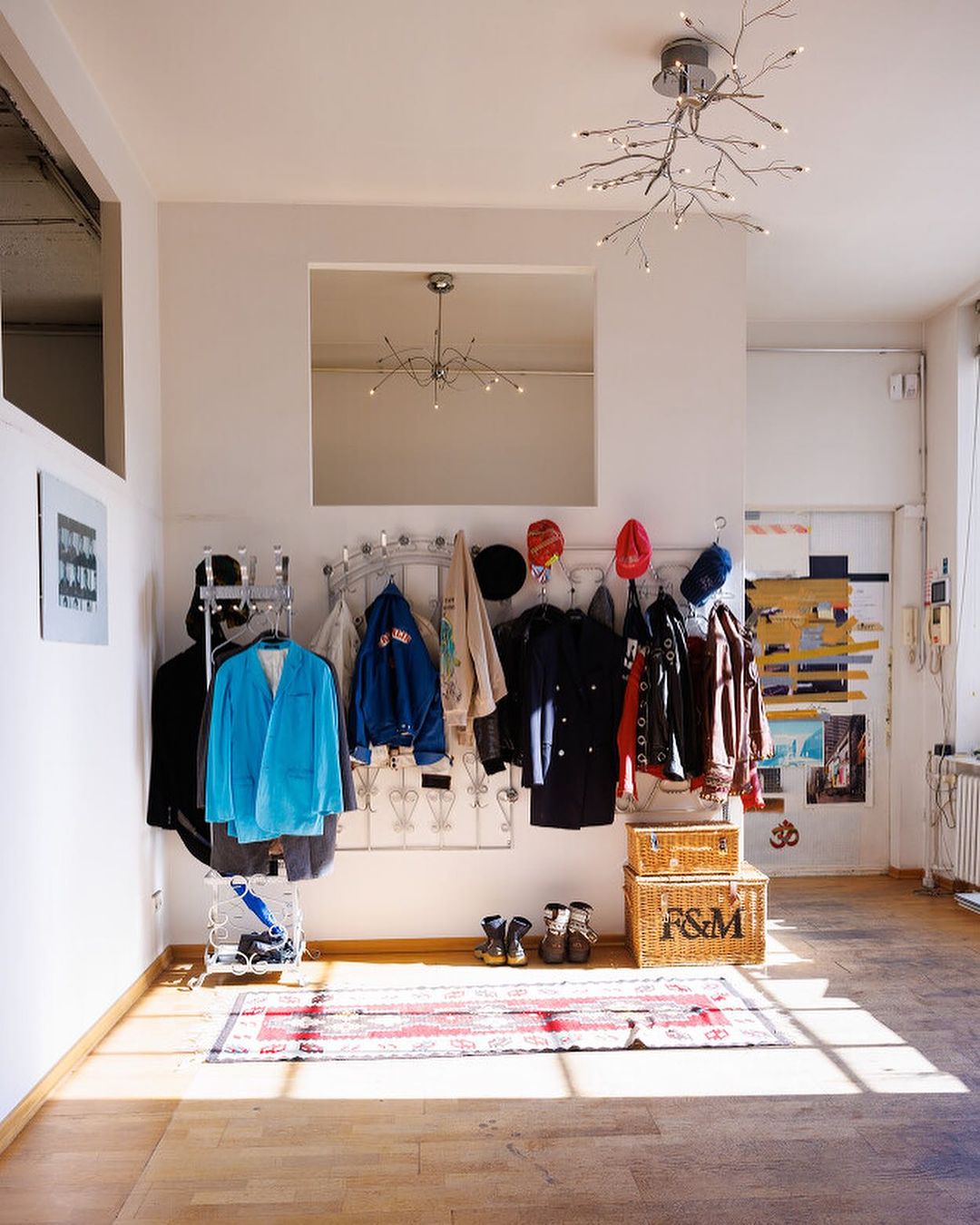 Hallway interior with clothing rack, hats, coats, baskets, a mirror, and a modern chandelier; natural light illuminates the wood flooring.