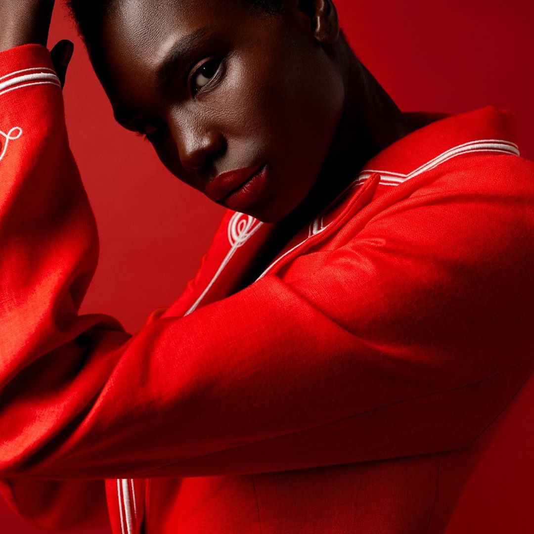 Close-up portrait of an adult female in a red jacket with white trim posing against a red background in a studio lighting setup.