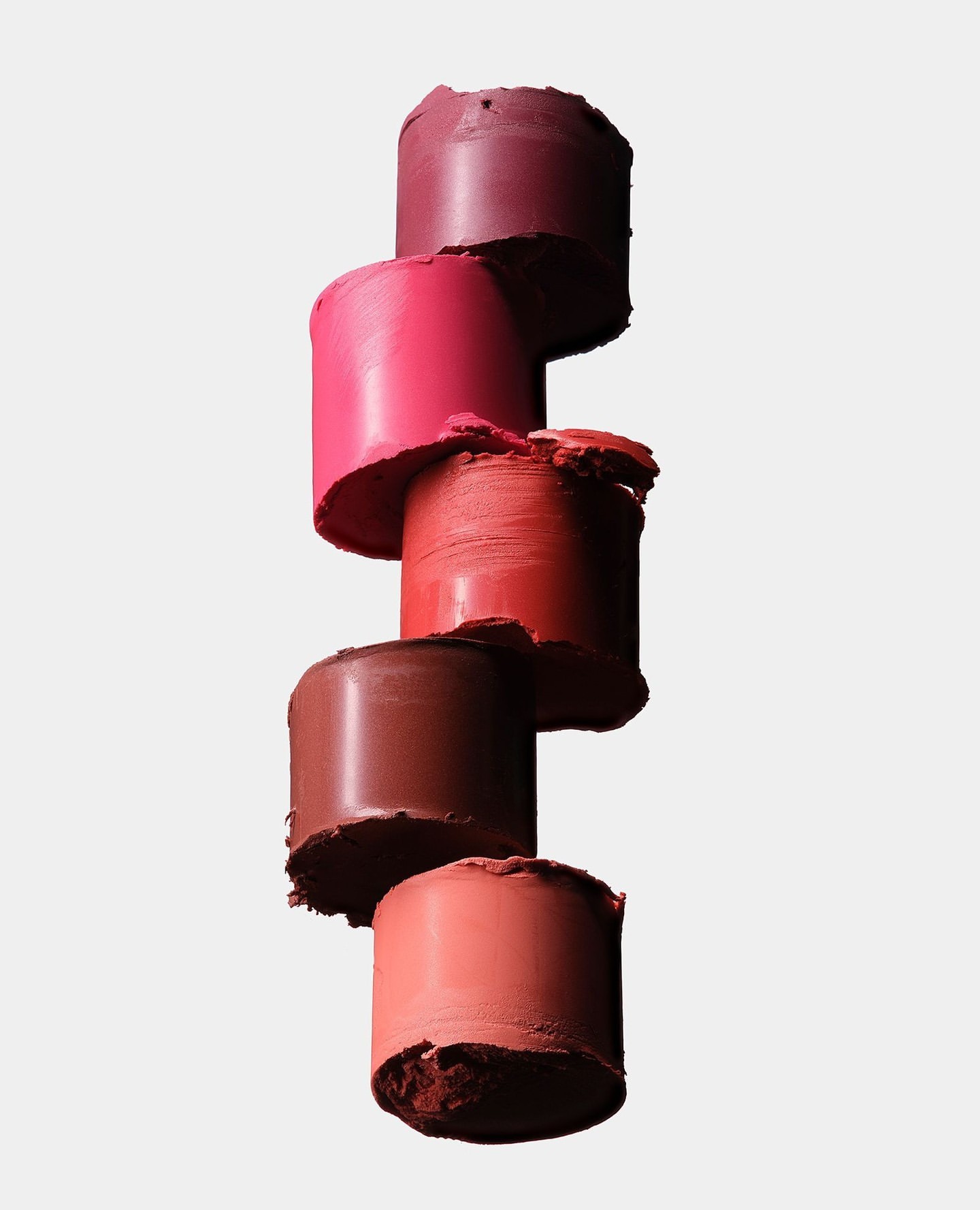 Stack of vibrant lipsticks in varying shades of red, pink, and brown, isolated against a light background, showcasing makeup textures.