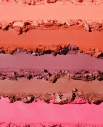 Horizontal swatches of cosmetic cream in shades of orange, terracotta, plum, brown, and pink with textured edges.