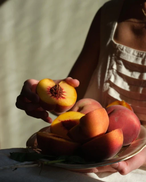 Woman holding a plate of fresh peaches indoors. Summer fruit still life photography. Healthy eating, fresh and juicy peach halves.