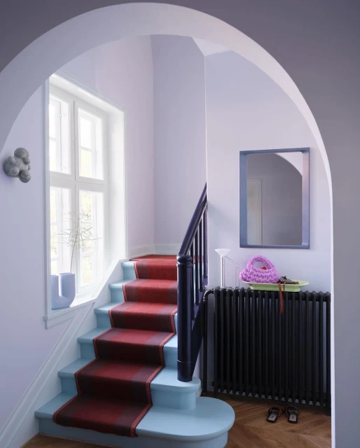 Interior view of a staircase with a red runner, leading up to a window with soft, natural light, and decorative accessories on a radiator shelf.