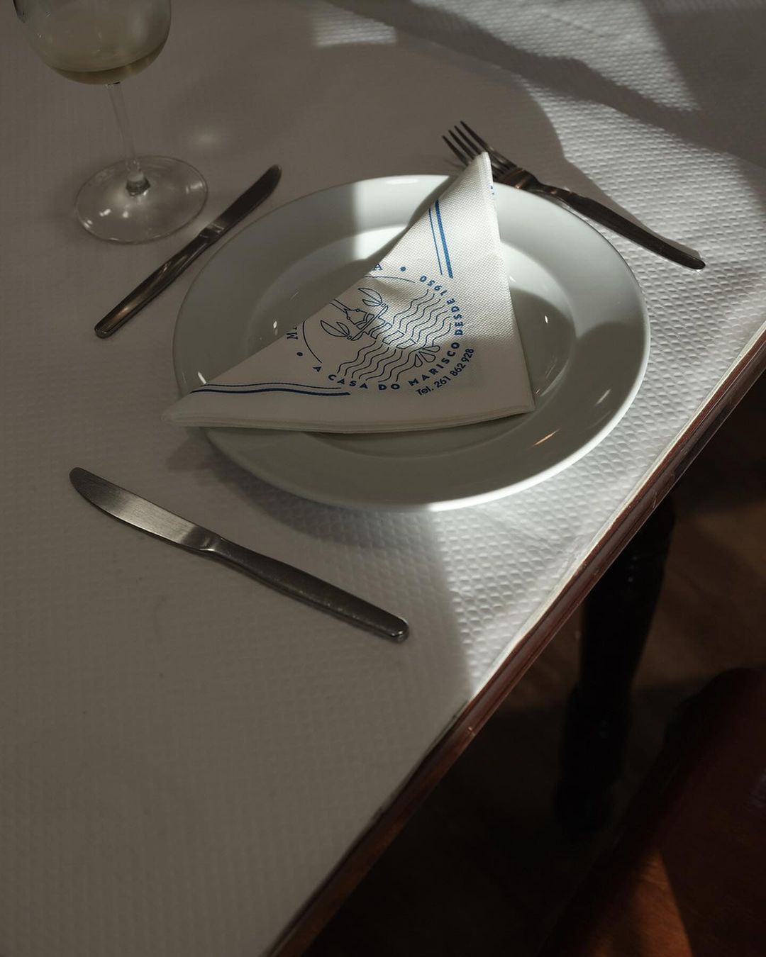 Overhead shot of a white plate with a patterned napkin, silverware, and a glass on a white tablecloth in a restaurant setting.