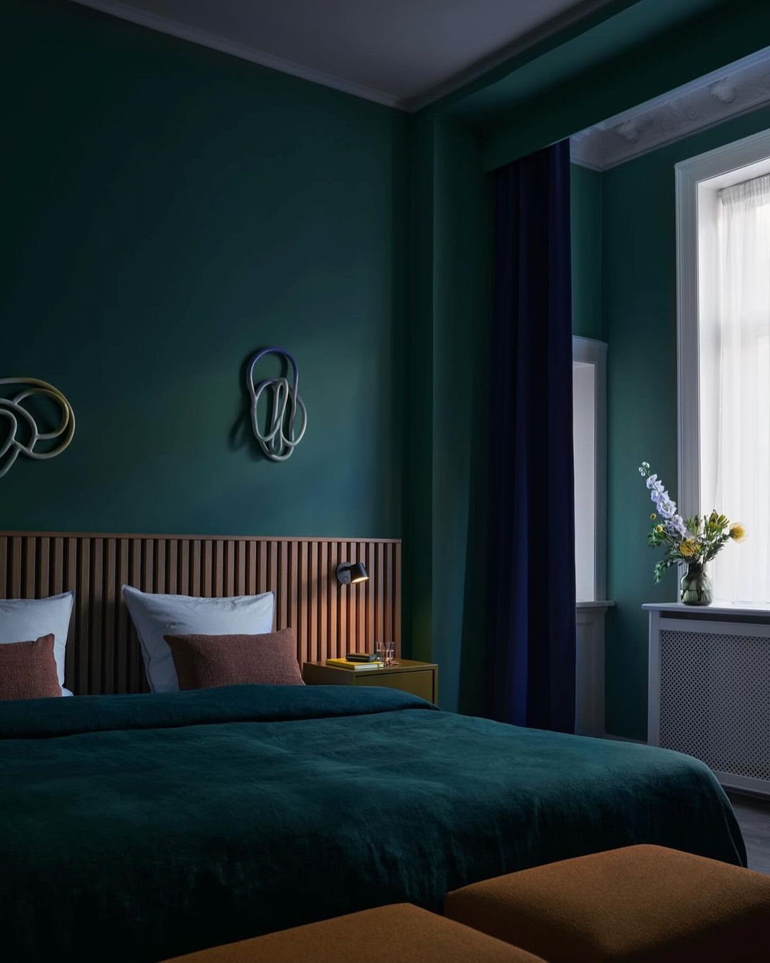 Bedroom in hotel room with a large bed, wooden headboard, vase of flowers, and abstract art on the wall in teal and dark blue tones.