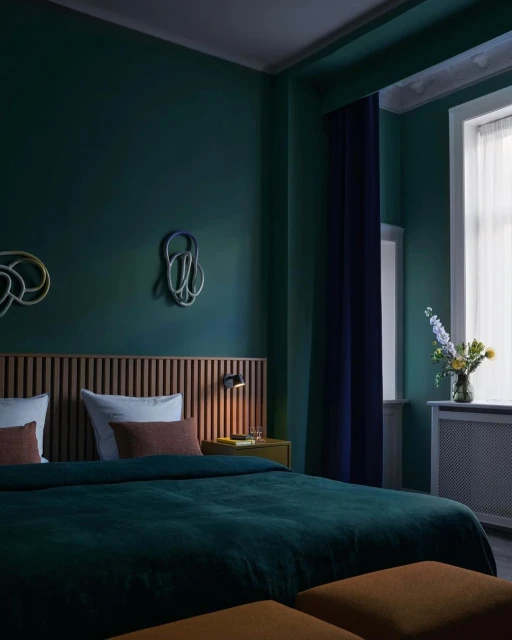 Bedroom in hotel room with a large bed, wooden headboard, vase of flowers, and abstract art on the wall in teal and dark blue tones.