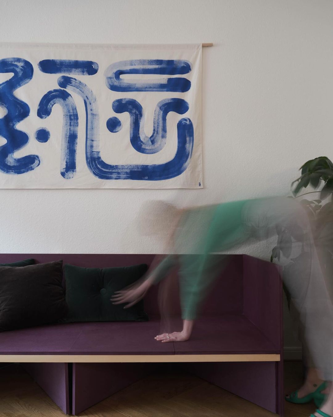 Interior shot of a living room with a person arranging cushions on a modern sofa, set against a backdrop of abstract wall art.