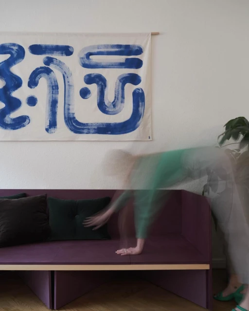 Interior shot of a living room with a person arranging cushions on a modern sofa, set against a backdrop of abstract wall art.