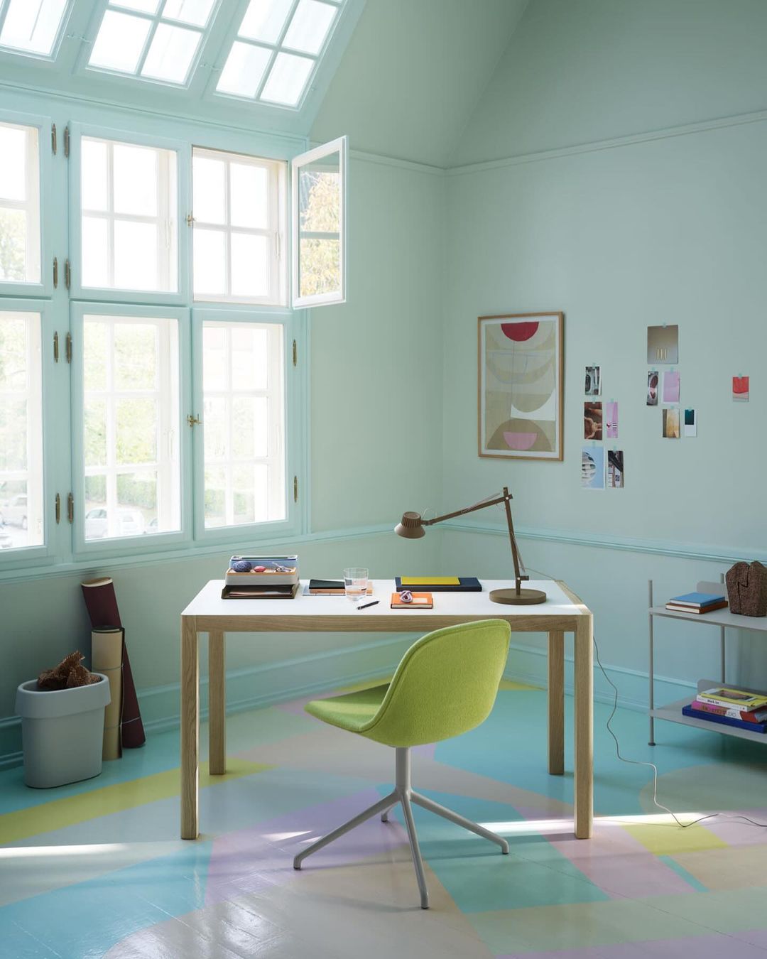 Interior design featuring a white desk with stationery, green chair, adjustable lamp, and sunlight shining through a multi-pane window.