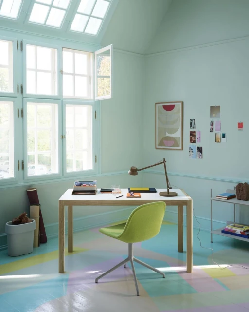 Interior design featuring a white desk with stationery, green chair, adjustable lamp, and sunlight shining through a multi-pane window.