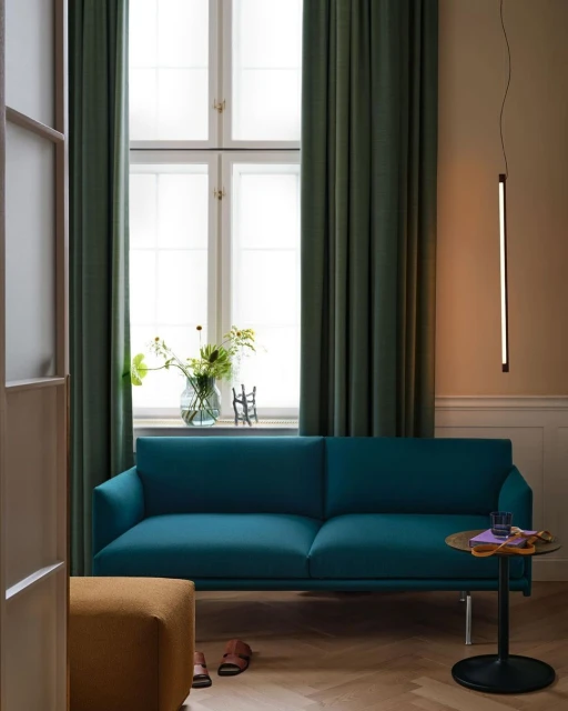 Teal colored couch situated in a living room near a window with green curtains, a modern lamp, and a small table in a home interior.