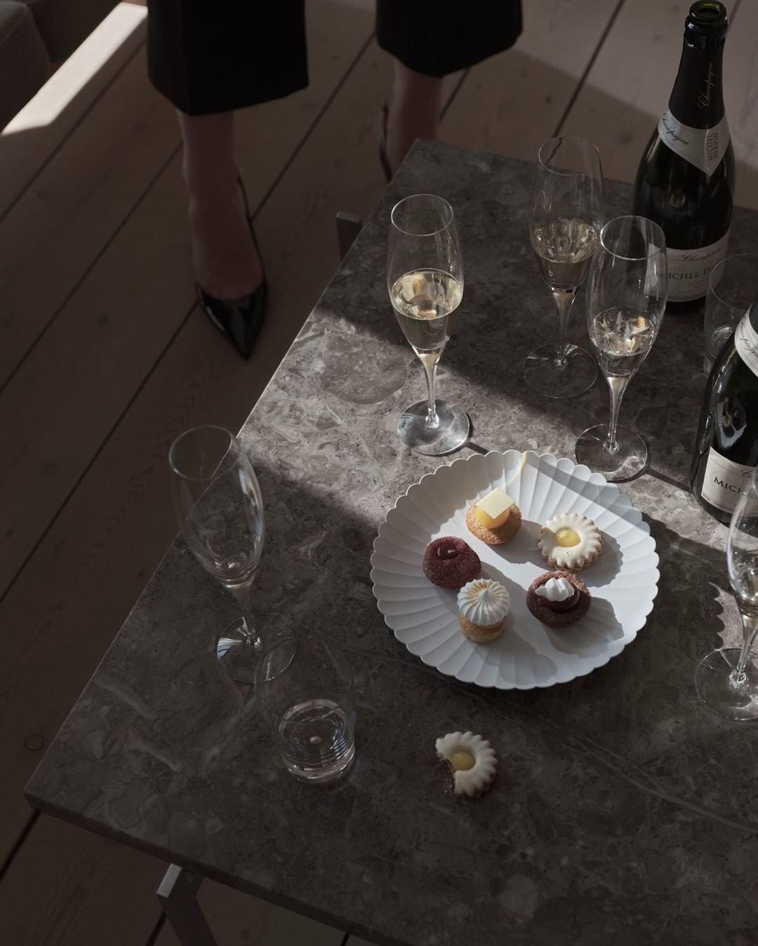 Still life featuring champagne flutes, champagne bottles, and an assortment of pastries elegantly arranged on a grey marble table.