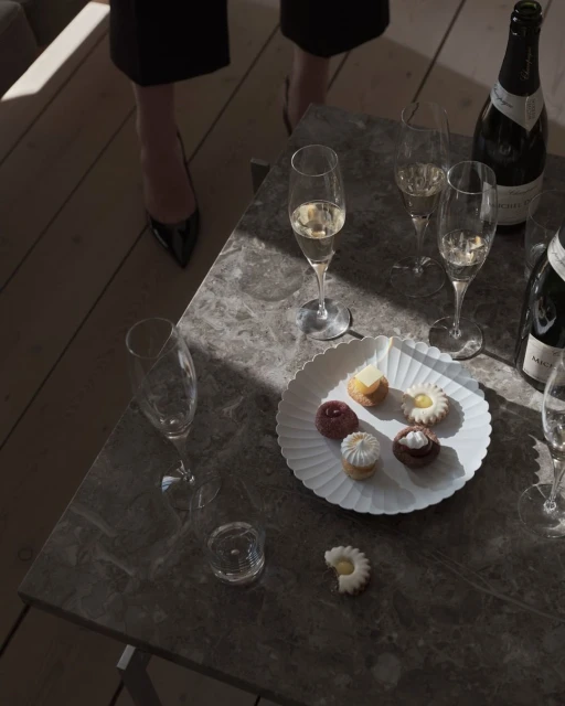 Still life featuring champagne flutes, champagne bottles, and an assortment of pastries elegantly arranged on a grey marble table.