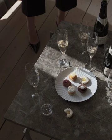Still life featuring champagne flutes, champagne bottles, and an assortment of pastries elegantly arranged on a grey marble table.