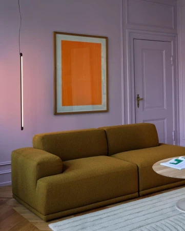 Living room interior featuring a mustard yellow sofa, artwork with an orange rectangle, and a minimalist floor lamp against a lilac wall.