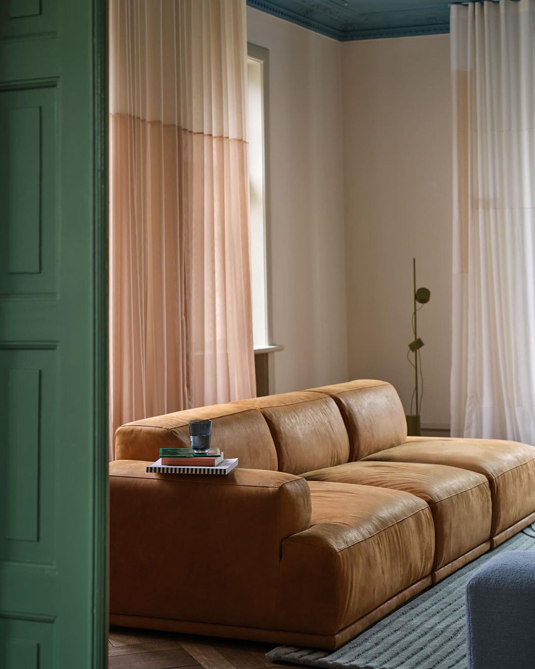Living room interior featuring a brown leather couch, window with beige curtains, and modern design elements against neutral wall.