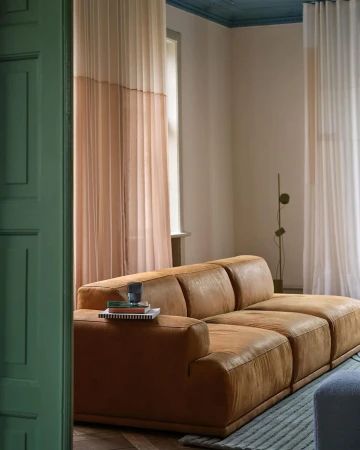 Living room interior featuring a brown leather couch, window with beige curtains, and modern design elements against neutral wall.