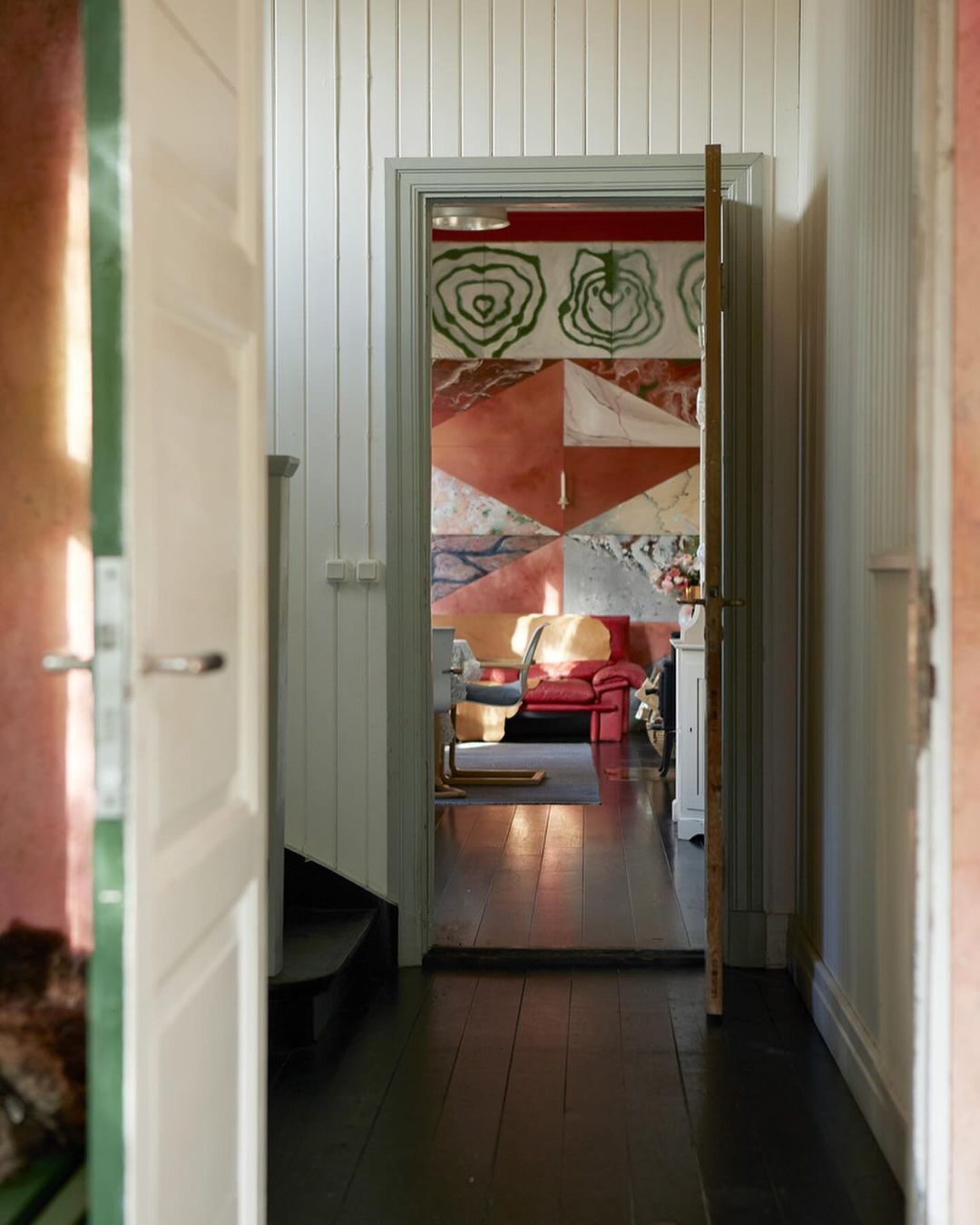 View through an open door into a room with geometric wall art, a red chair, and dark wood floors, captured in a medium indoor shot.