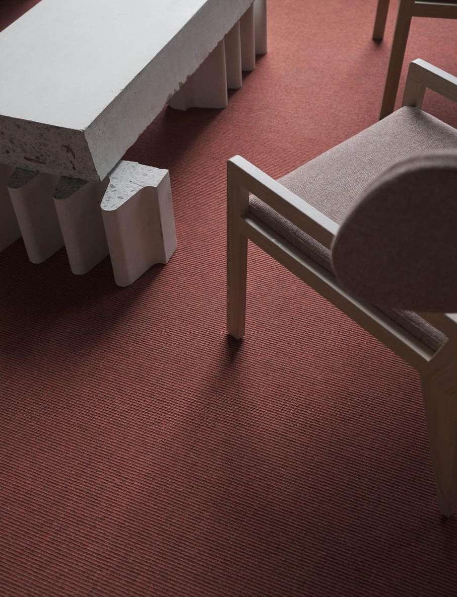 Beige fabric chair next to a light gray table and a salmon-colored carpet, capturing a minimalist design and focus on texture.