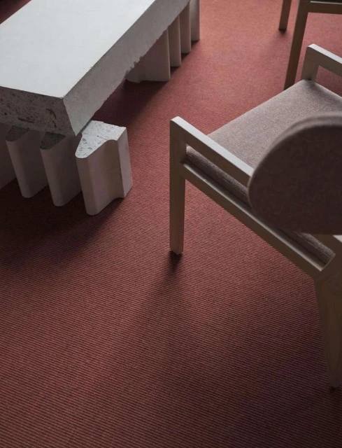 Beige fabric chair next to a light gray table and a salmon-colored carpet, capturing a minimalist design and focus on texture.