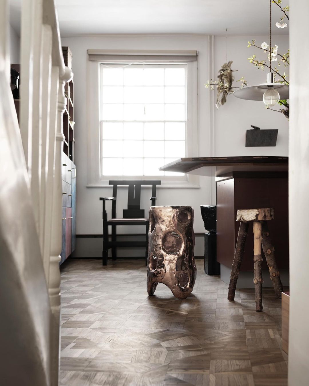 Interior view of a modern room with an artistic stool, wooden floor, window, and a desk, creating a cozy and contemporary atmosphere.