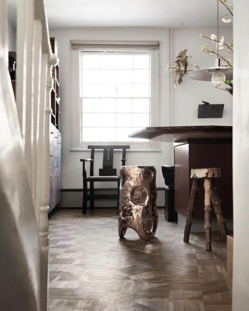 Interior view of a modern room with an artistic stool, wooden floor, window, and a desk, creating a cozy and contemporary atmosphere.