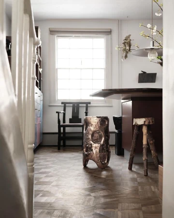 Interior view of a modern room with an artistic stool, wooden floor, window, and a desk, creating a cozy and contemporary atmosphere.