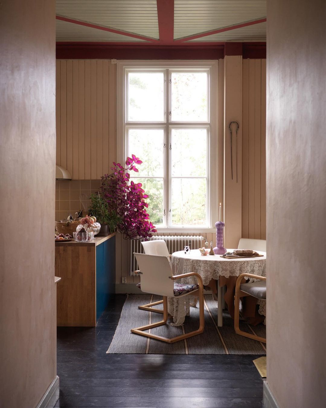 Interior shot of a dining area with a round table, chairs, and flowers, featuring neutral wall tones and natural light from a window.