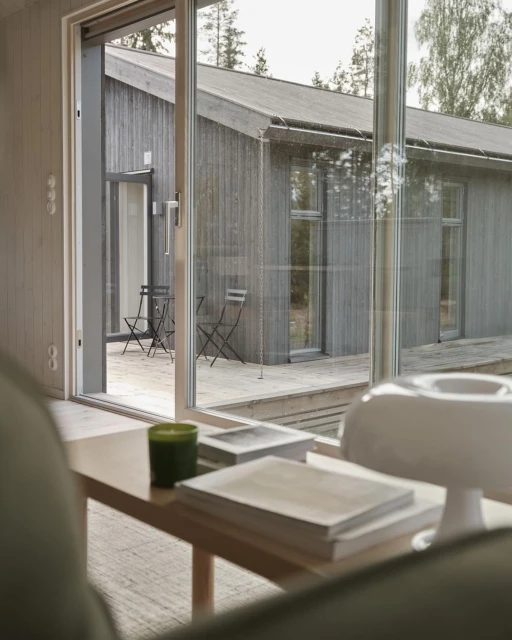 Interior shot of a modern home with a living room featuring a wooden table with books, a lamp, and an open view to a terrace.
