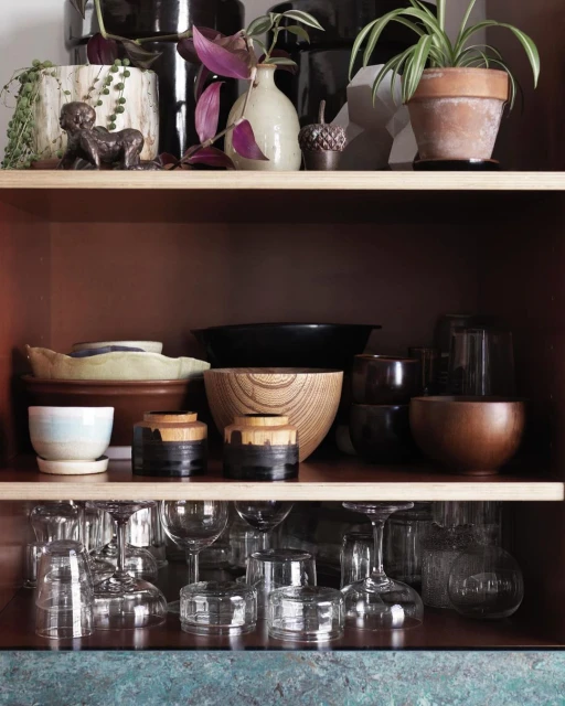 Shelves with plants and pottery, including ceramic pots, glass goblets and bowls in neutral and earth-tone colors.