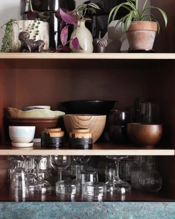 Shelves with plants and pottery, including ceramic pots, glass goblets and bowls in neutral and earth-tone colors.
