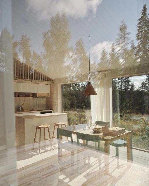 Light and airy kitchen and dining area with modern wood furniture, large windows, and a view of a forest, creating a bright, natural atmosphere.
