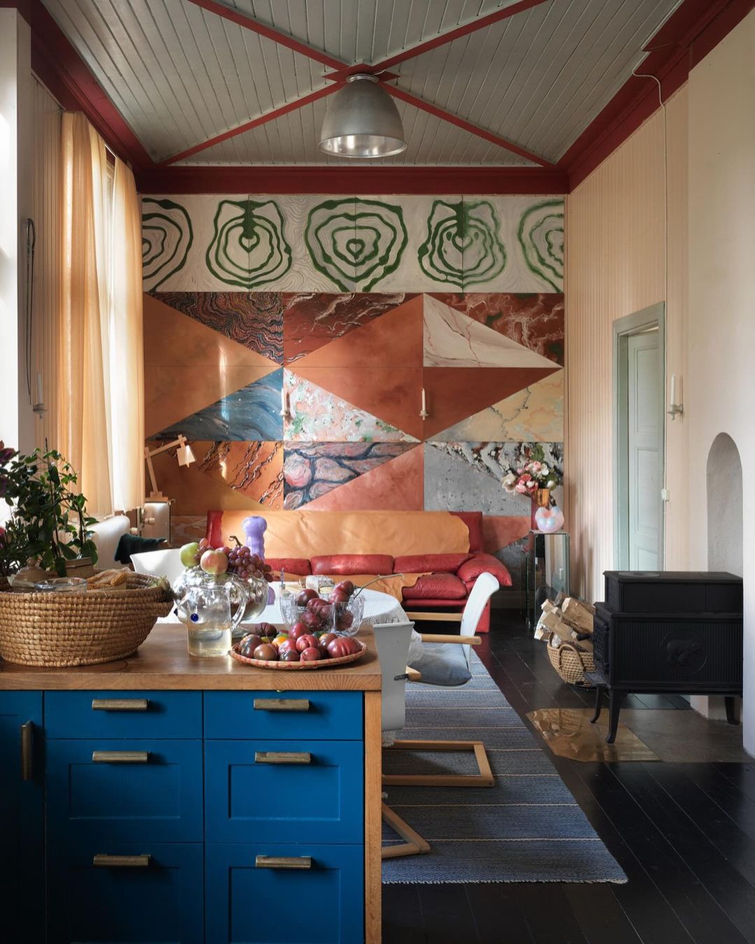 Living room interior with geometric wall art, blue cabinets, wooden accents, and a mix of vintage and modern decor elements.
