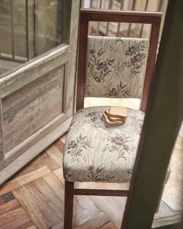 Floral chair with bread on a glass plate indoors. Rustic wooden door and herringbone floor create a vintage aesthetic.