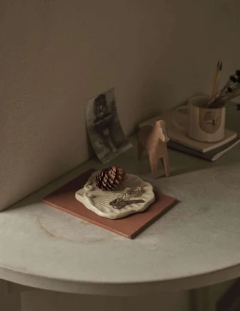 Still life of a pine cone, keys, and a wooden horse figurine on a table with a photo and a mug in the background.