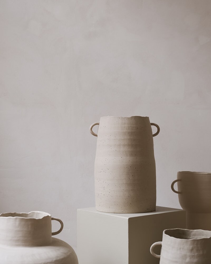 Still life shot of a collection of beige handmade ceramic vases on a neutral beige background indoors with soft, diffused natural light.