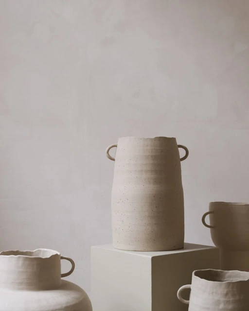 Still life shot of a collection of beige handmade ceramic vases on a neutral beige background indoors with soft, diffused natural light.