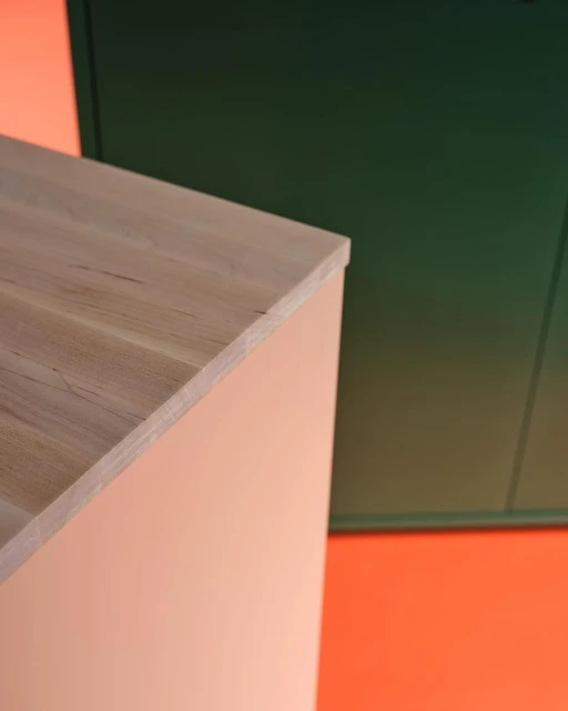 Minimalist geometric interior shot of a light wood cabinet and dark green panel against a peach and orange background.