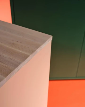 Minimalist geometric interior shot of a light wood cabinet and dark green panel against a peach and orange background.