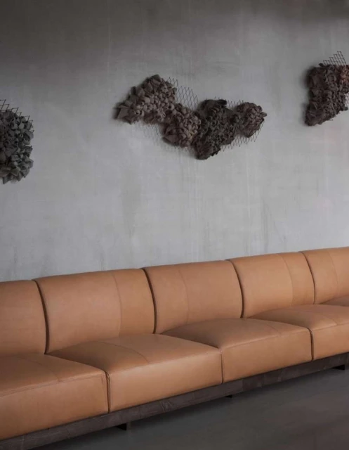 Interior view of a contemporary lounge area with a tan leather sofa against a gray wall featuring textured art pieces.