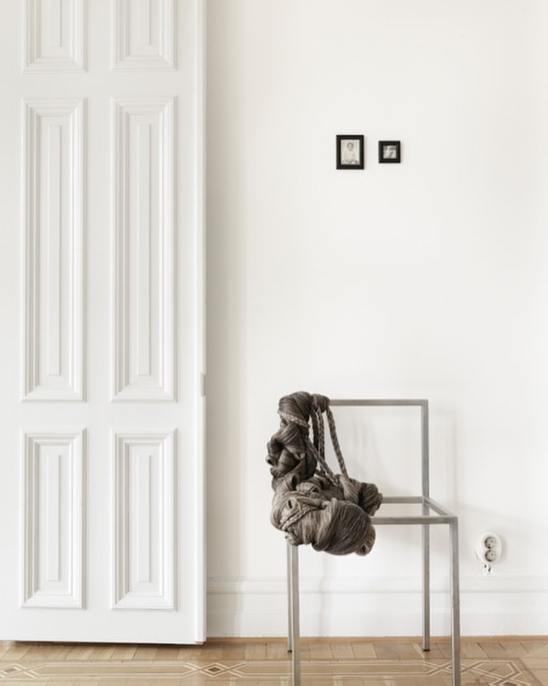 Minimalist interior with white walls, wooden floor, and a modern silver chair draped with a taupe knotted rope decoration or bag.