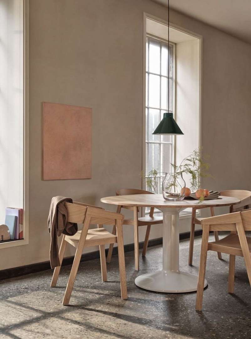 Interior design showcasing a round wooden dining table with light wood chairs, set against a neutral wall with artwork and window light.