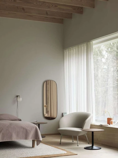 Bright, minimalist bedroom interior with soft light. Modern chair, bed, floor rug, and wall mirror create a serene, inviting space.