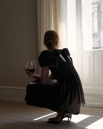 Woman in black dress crouching near a window holding a wine glass by photographer Petra Bindel