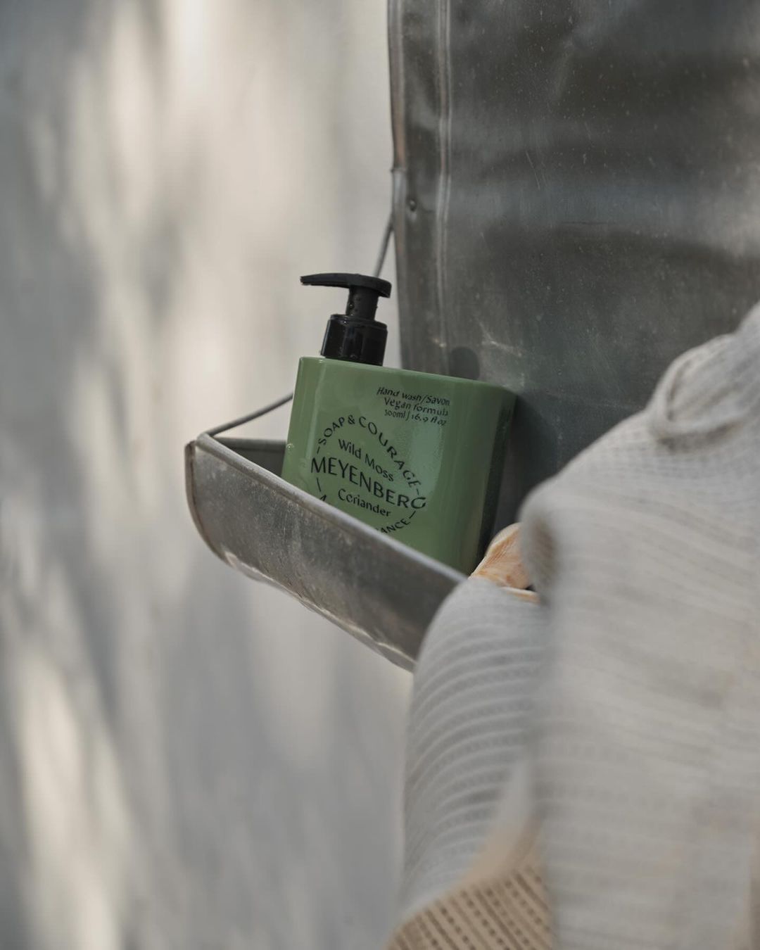 Bottle of soap sits on a metal shelf with knitted sweater in the foreground, showcasing cleanliness, self-care, and home organization.