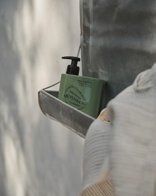 Bottle of soap sits on a metal shelf with knitted sweater in the foreground, showcasing cleanliness, self-care, and home organization.